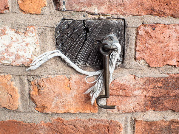 a rusty key on a wooden block insterted in a brick wall with a thick piece of string hanging from it.